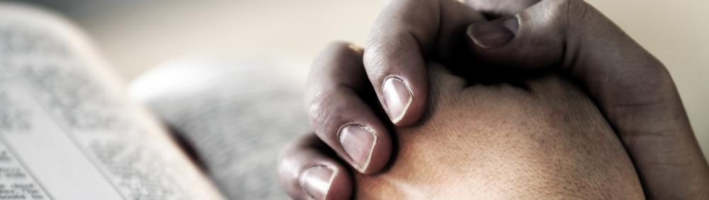 hands clasped in prayer over Bible