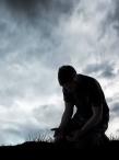 Man kneeling under dark clouds praying