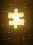 A golden, glowing piece of a jigsaw puzzle, fitted neatly among its darkly-colored jigsaw-puzzle-piece compatriots