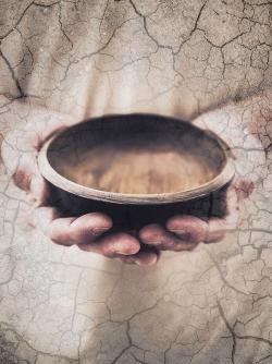 Hands holding an empty bowl on cracked ground hunger concept