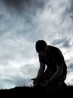 Man kneeling under dark clouds praying