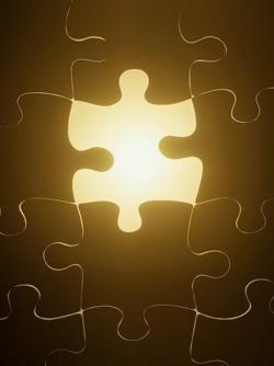 A golden, glowing piece of a jigsaw puzzle, fitted neatly among its darkly-colored jigsaw-puzzle-piece compatriots