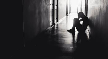 teenager holding his head in his hands sitting in a dark hallway