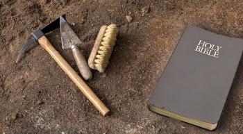 archaeological tools and a Bible laying on the dirt