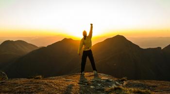 person overlooking mountain scenery with fist raised in air triumphantly