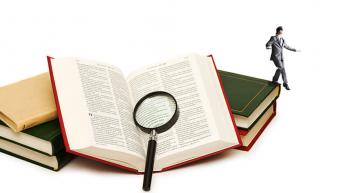 A tiny blindfolded man walking off of a stack of books, one of which is an open Bible with a magnifying glass resting on it