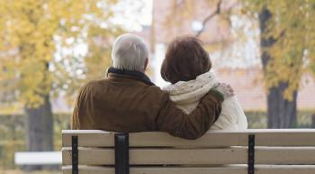 An elderly couple sitting on a park bench in Autumn with their backs to the viewer