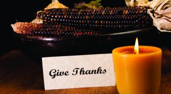 "Give Thanks" sign in setting with corn cobs and glowing candle