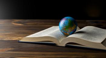 An open Bible on a table with a globe of earth resting in the center.