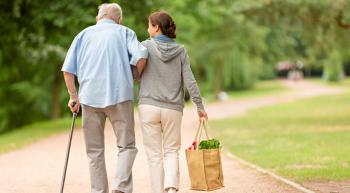 A woman helping an elderly man walk down a road