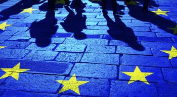 cobblestone street with shadows of migrants approaching a circle of yellow stars representing the European Union