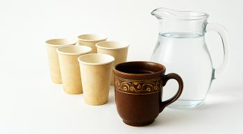 An ornate mug, flanked by dirty paper cups and a clear glass pitcher of water.