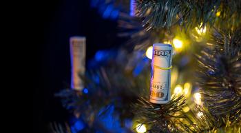 A lit Christmas tree with rolls of 100 dollar bank notes hanging from it in place of decorations.