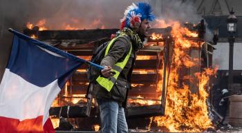 man waving French flag in front of a burning stack of pallets