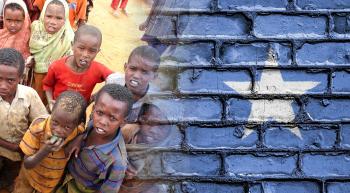 Somalian kids with serious faces next to a brick wall painted like the flag of Somalia