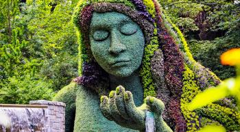 a floral sculpure of a woman with water flowing out of the palm of her hand