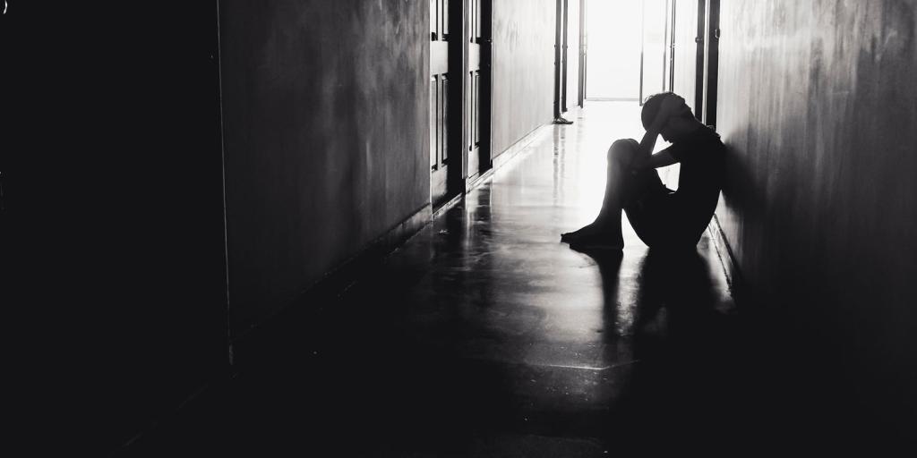 teenager holding his head in his hands sitting in a dark hallway