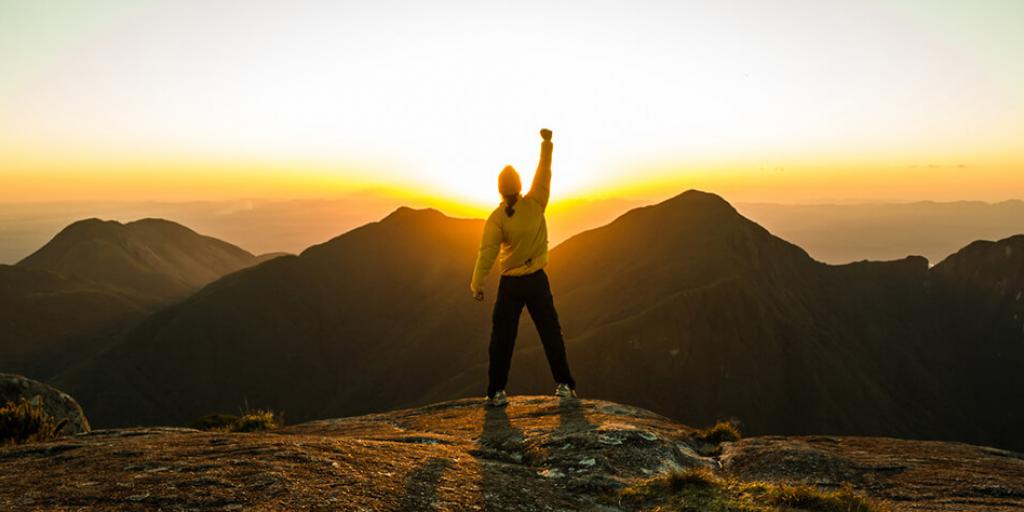 person overlooking mountain scenery with fist raised in air triumphantly