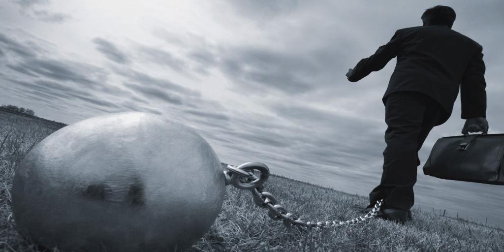 man holding breifcase with a chain around his ankle attached to a heavy ball