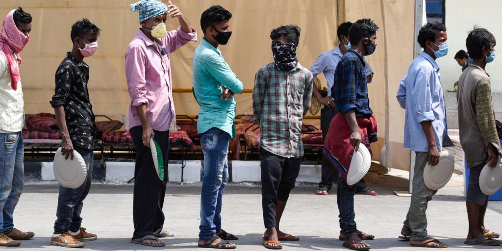 men wearing masks and waiting in line for food