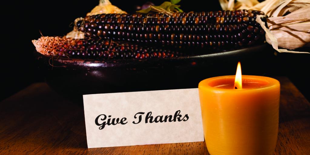 "Give Thanks" sign in setting with corn cobs and glowing candle