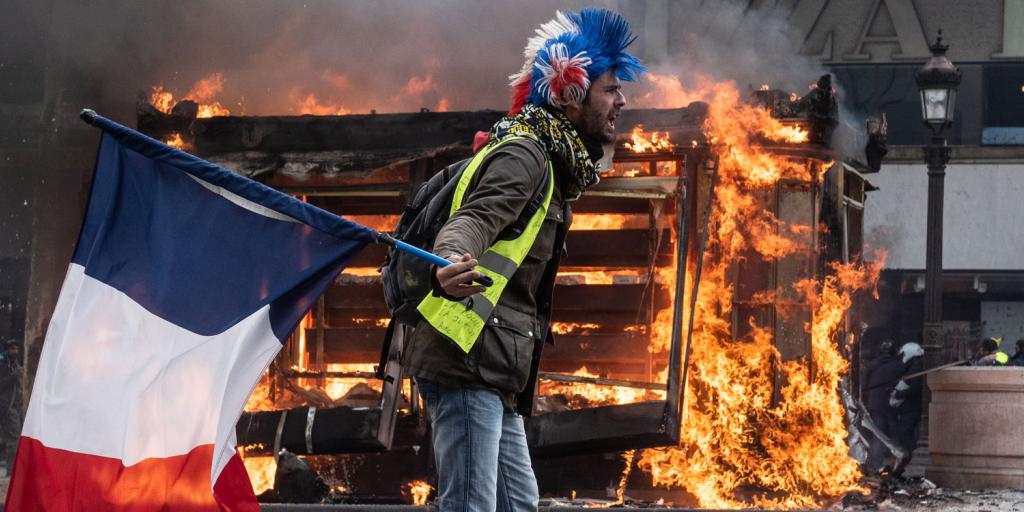 man waving French flag in front of a burning stack of pallets