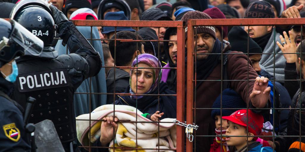 large crowd of migrants attempting to enter Slovenia at a padlocked gate