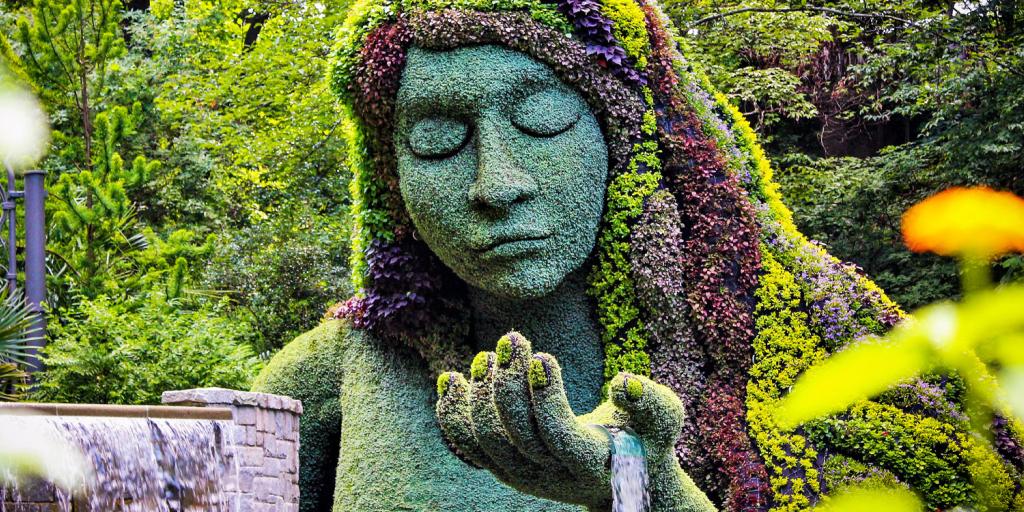 a floral sculpure of a woman with water flowing out of the palm of her hand