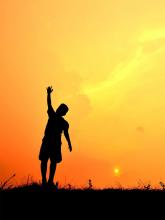 Boy with arm raised against orange sunset