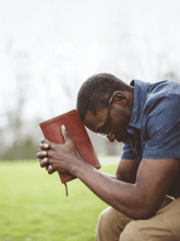 Man holding a Bible praying intently in an outdoor setting