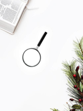 A magnifying glass between a Bible and a tree that looks Christmas-like