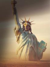 The Statue of Liberty rises from a barren, dusty landscape, partially buried in sand with its torch raised against a hazy, dramatic sky.