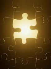 A golden, glowing piece of a jigsaw puzzle, fitted neatly among its darkly-colored jigsaw-puzzle-piece compatriots