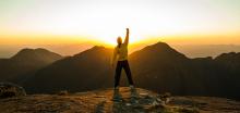 person overlooking mountain scenery with fist raised in air triumphantly