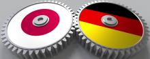 two gears meshed together, one depicting the Japanese flag the other the German flag