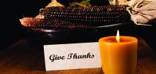 "Give Thanks" sign in setting with corn cobs and glowing candle