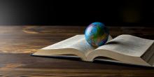 An open Bible on a table with a globe of earth resting in the center.