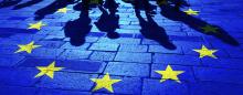 cobblestone street with shadows of migrants approaching a circle of yellow stars representing the European Union