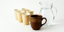 An ornate mug, flanked by dirty paper cups and a clear glass pitcher of water.