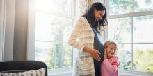a pregnant woman smiling as a young girl leans against her belly, listening with excitement