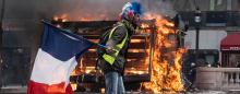 man waving French flag in front of a burning stack of pallets