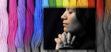 Woman praying, slowly turning from black and white into color, with stripes of vivid color in the background, fading from grey to rainbow shades.