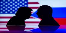 black silhouette cutouts of Donald Trump and Vladimir Putin facing each other, with the flags of the United States and Russia in the background