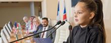 young girl at a podium speaking in front of adults